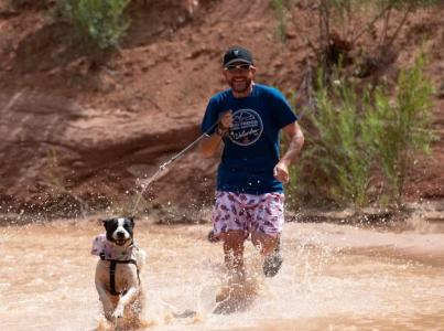 Smiling person running next to a dog through a Southwest Utah creek